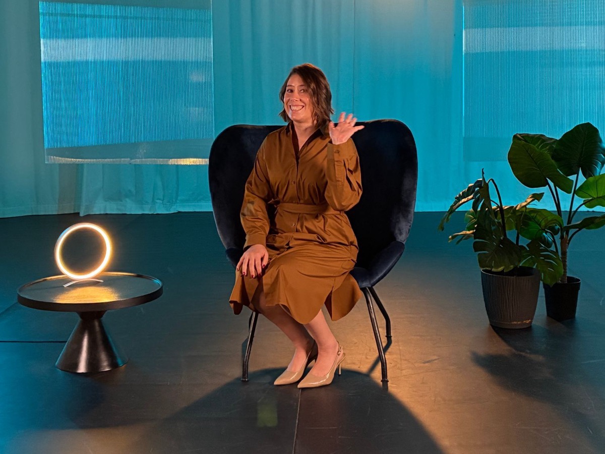Cristina Peñaloza waving from a studio set during a recording